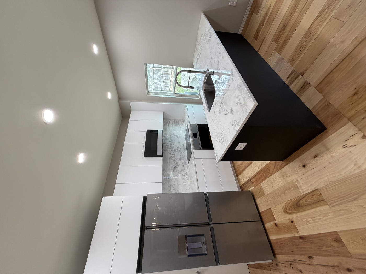 Remodeled white kitchen with marble-top island, stainless fridge, and hardwood floors