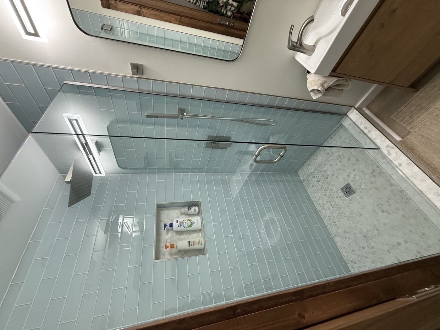 Frameless glass shower with sky-blue subway tile and marble-look shower pan
