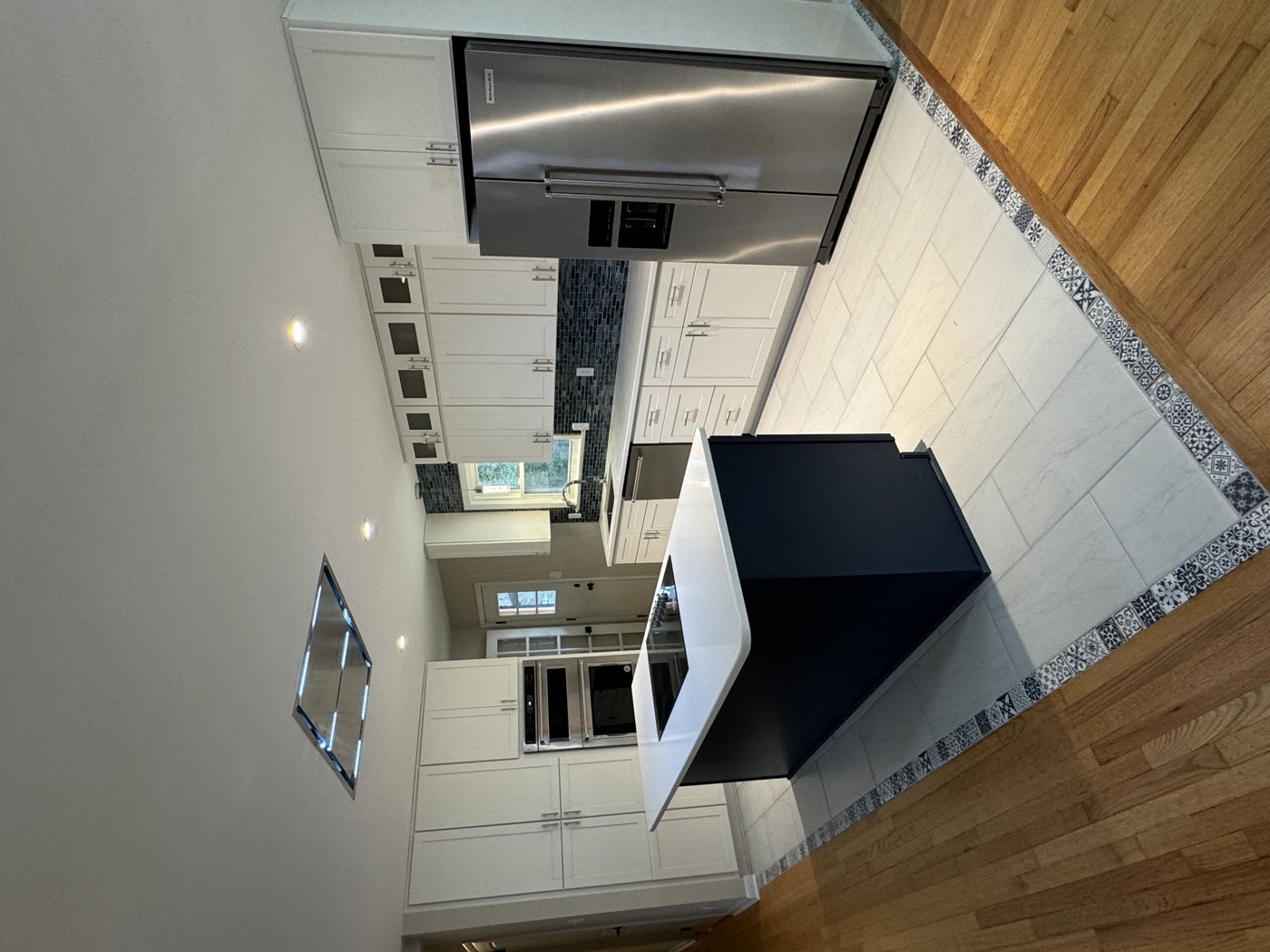 White shaker kitchen with navy blue island, double wall ovens, and tile floor with decorative border