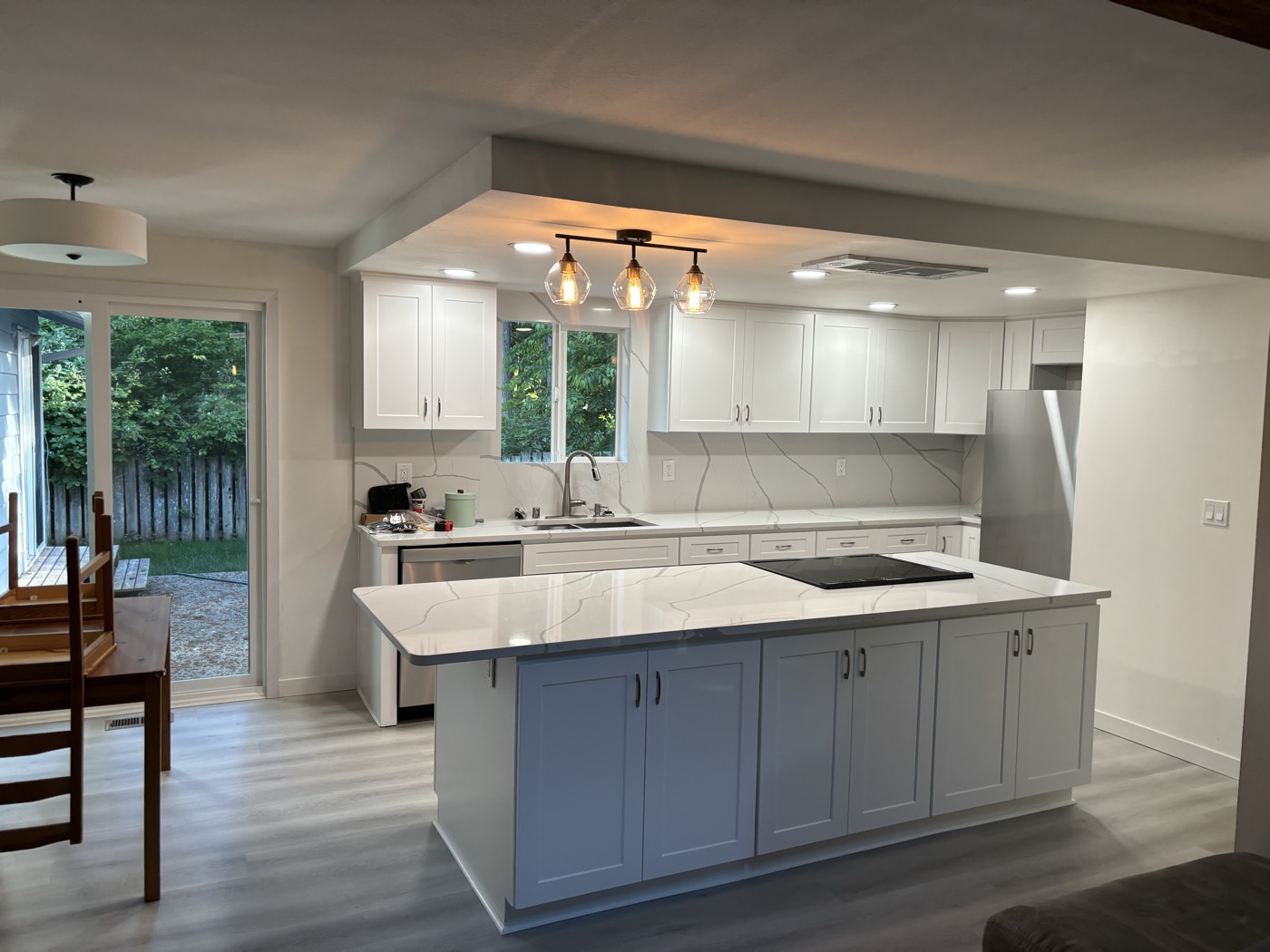 Open-concept white shaker kitchen with large island, cooktop, and backyard view