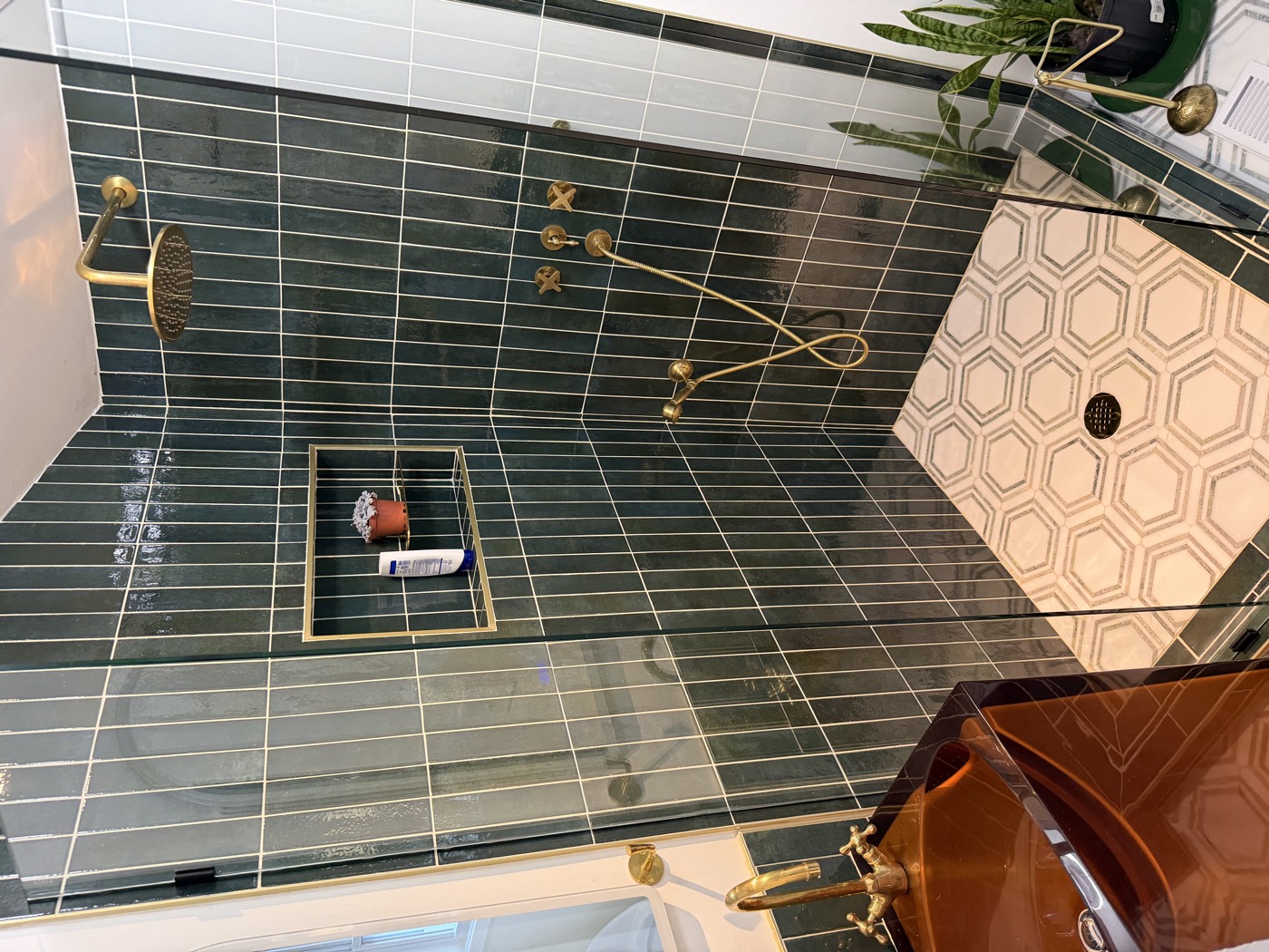 Walk-in shower with green vertical tile, brass fixtures, and hexagon mosaic floor